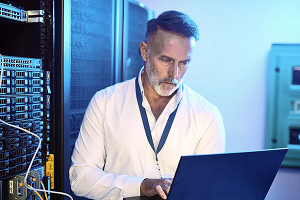 Shot of a mature man using a laptop while working in a server room